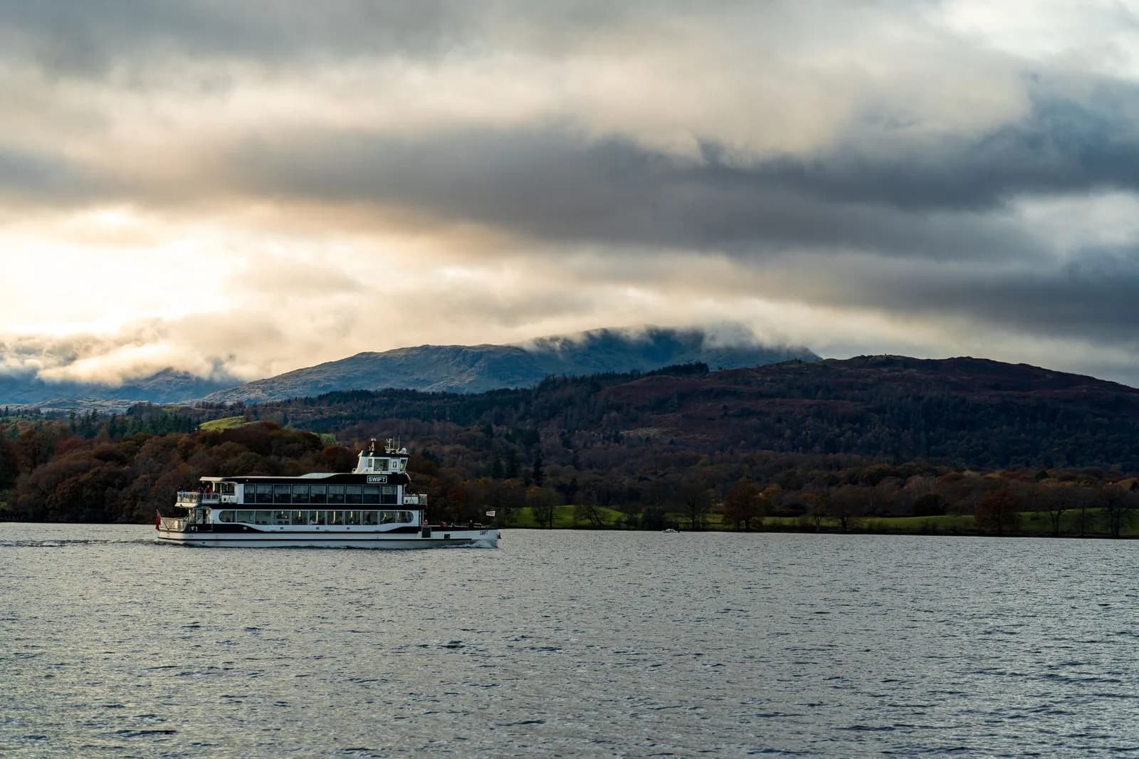 Bateau de croisière sur un lac du Lake District devant des collines boisées