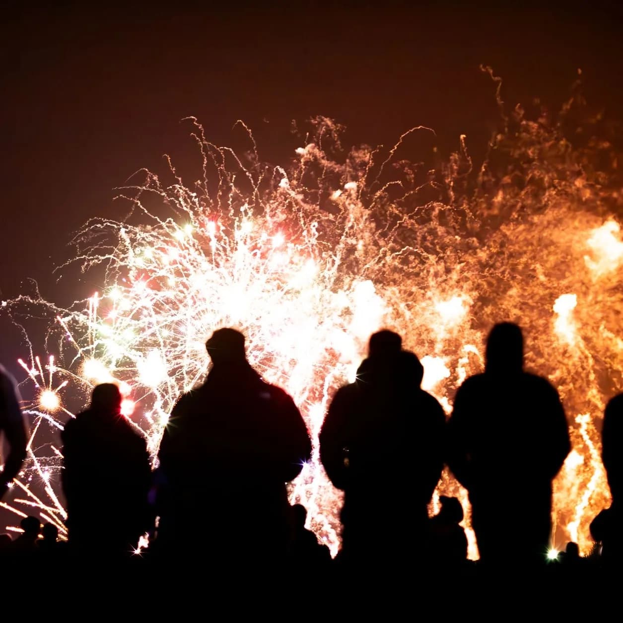 Foule en silhouette devant des flammes orangées et un feu d'artifice, de nuit