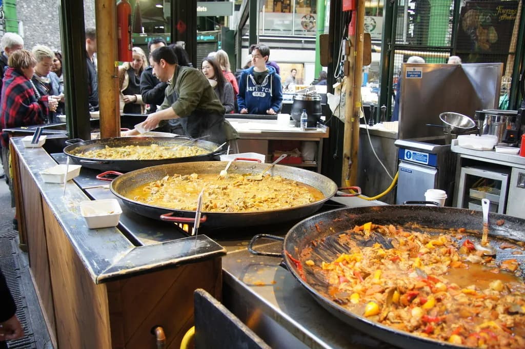 Cuisiniers devant de grandes poêles de plats chauds sur un stand de cuisine de rue à Borough Market