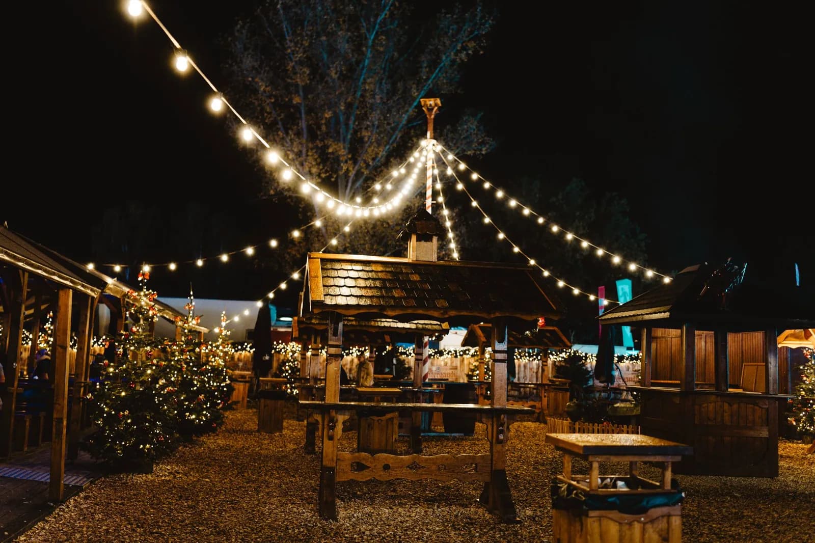 Chalets en bois d'un marché de Noël illuminés à la nuit tombée sous des guirlandes
