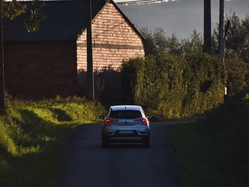 Citadine grise roulant sur une petite route de campagne anglaise bordée de haies, près d'une grange en briques