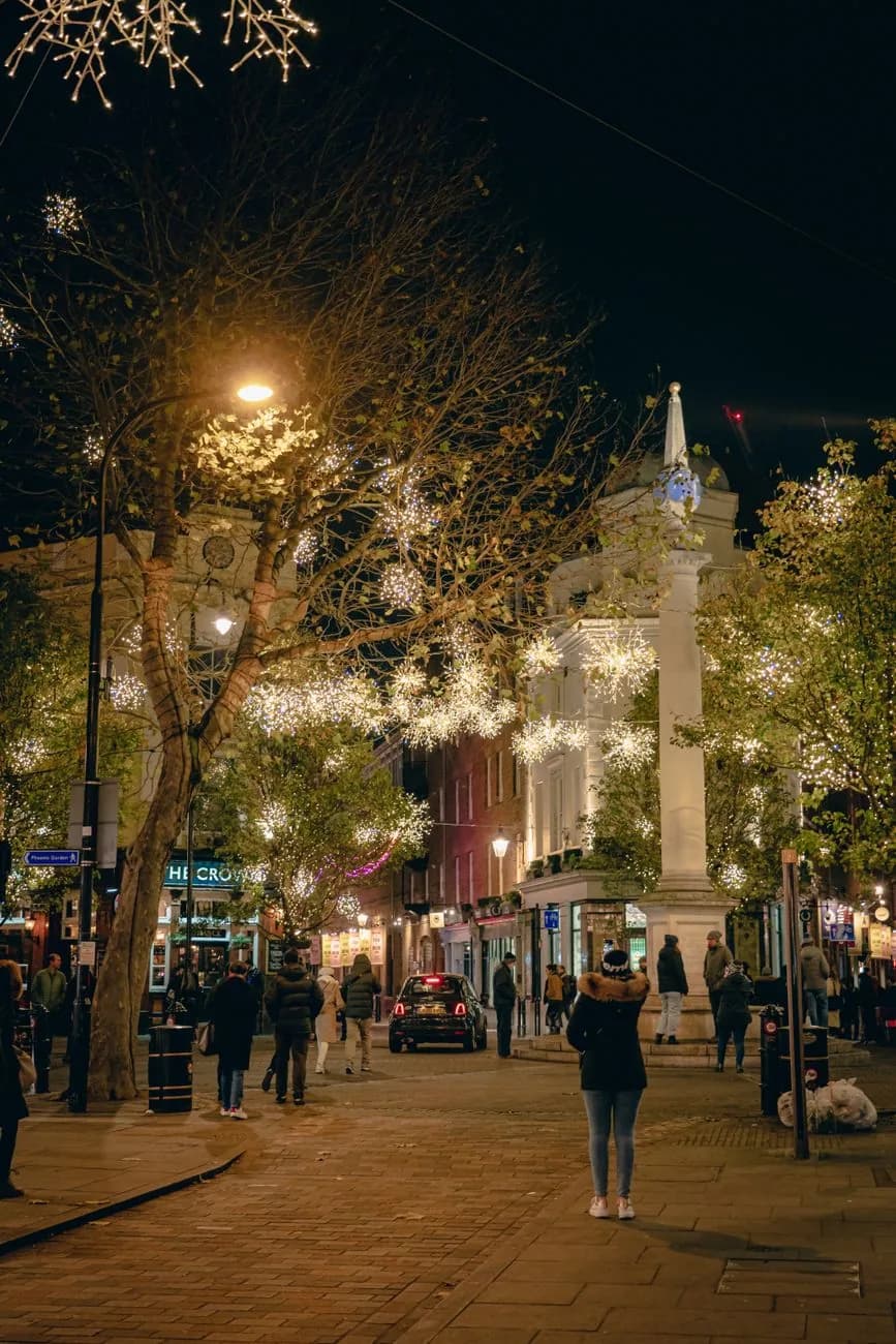 La colonne de Seven Dials éclairée de nuit, entourée d'arbres ornés de guirlandes lumineuses