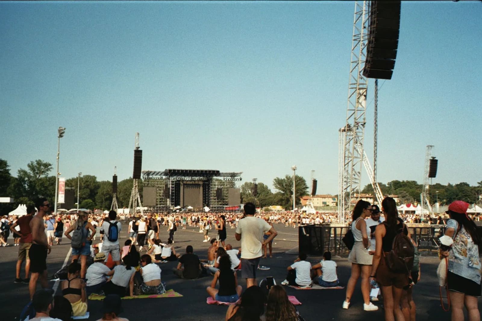 Foule devant une grande scène de concert en plein air, sous un ciel bleu d'été
