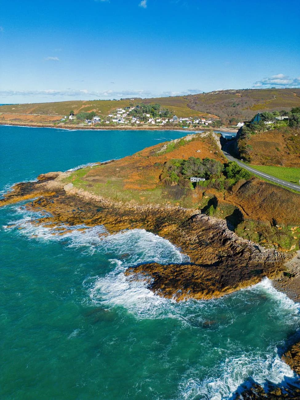 Côte rocheuse des Cornouailles avec un village au-dessus d'une baie turquoise