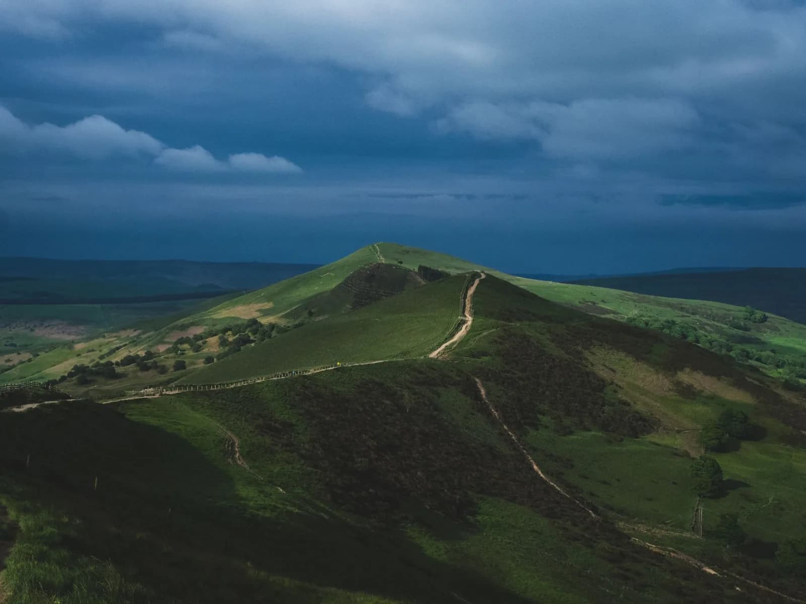 Sentier dallé sur une crête herbeuse du Peak District, sous un ciel d'orage