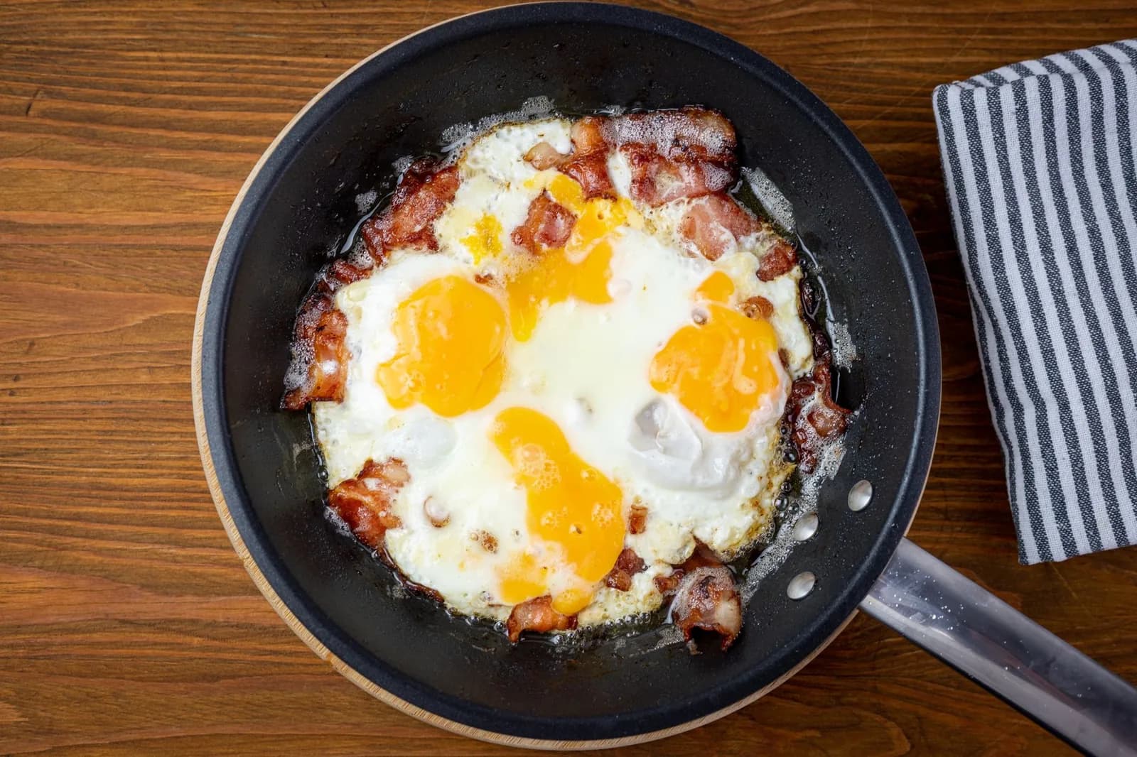 Bacon et œufs au plat en train de cuire dans une poêle noire, vus de dessus