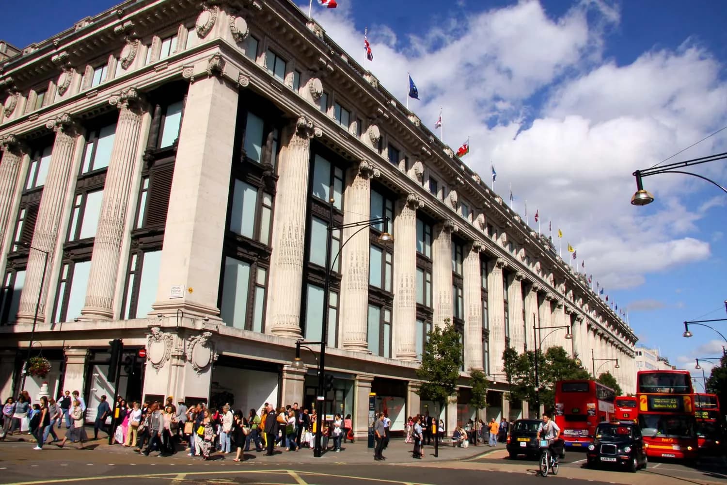 Façade à colonnes du grand magasin Selfridges sur Oxford Street à Londres, avec des drapeaux et des passants