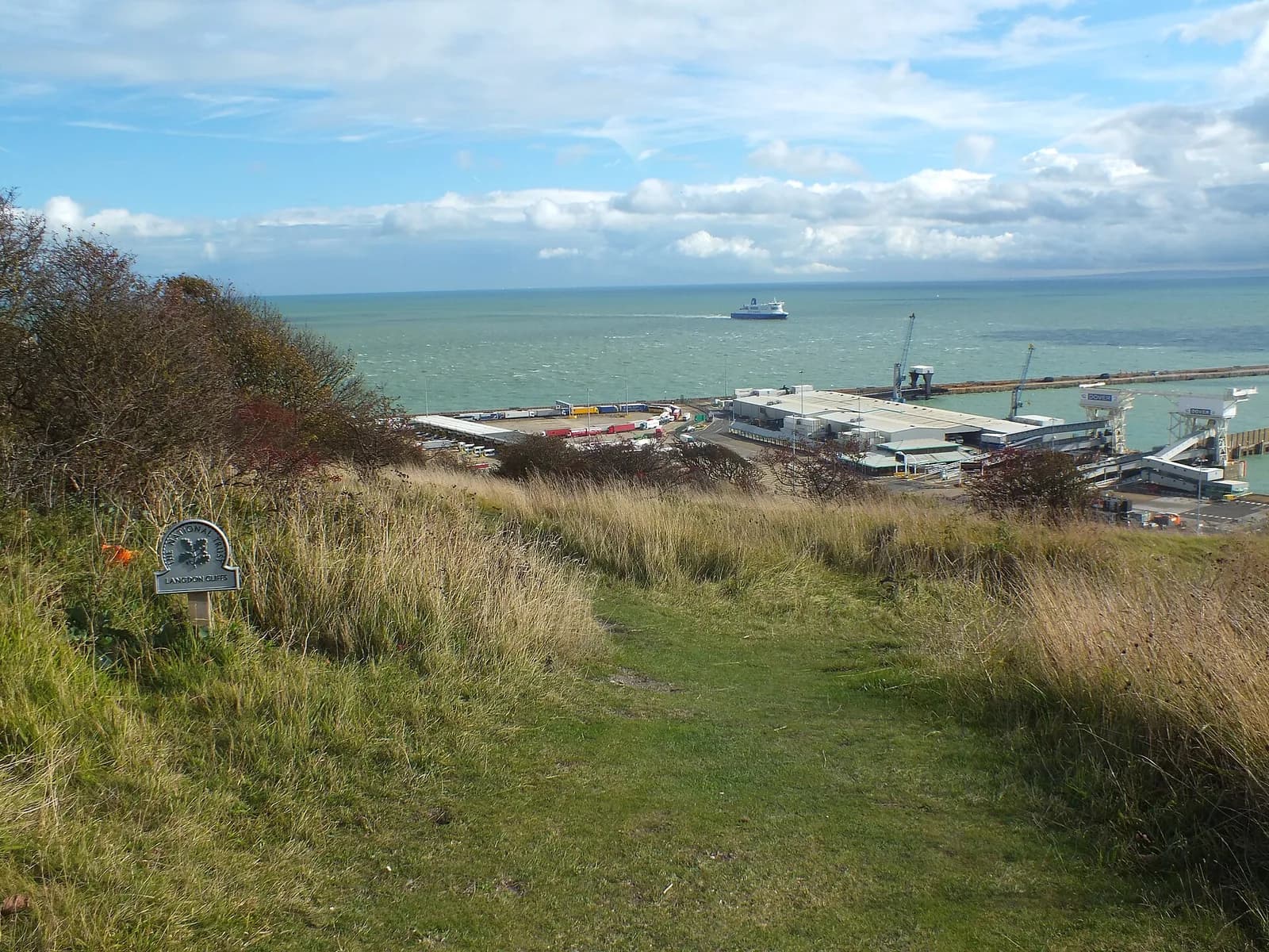 Sentier herbeux sur les hauteurs de Langdon Cliffs, avec un panneau du National Trust et vue sur le port de Douvres