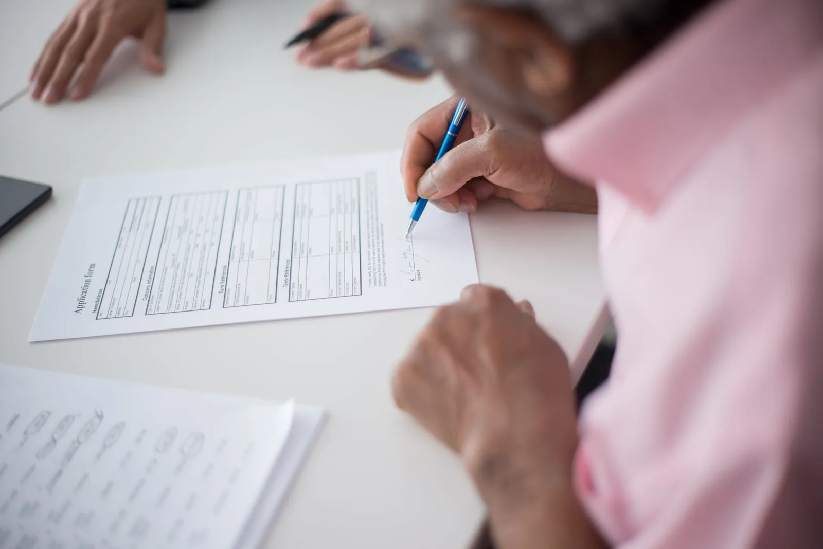 Une personne remplit un formulaire de demande avec un stylo, à une table de travail