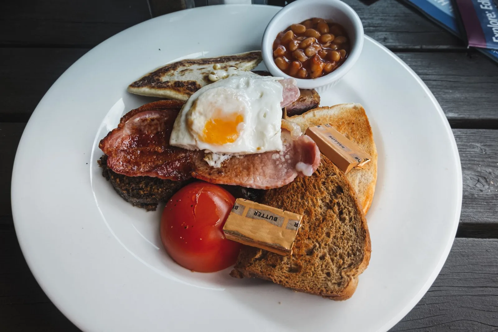 Assiette de petit-déjeuner anglais complet : bacon, œuf au plat, tomate, haricots blancs à la sauce tomate et toasts, sur une table en bois
