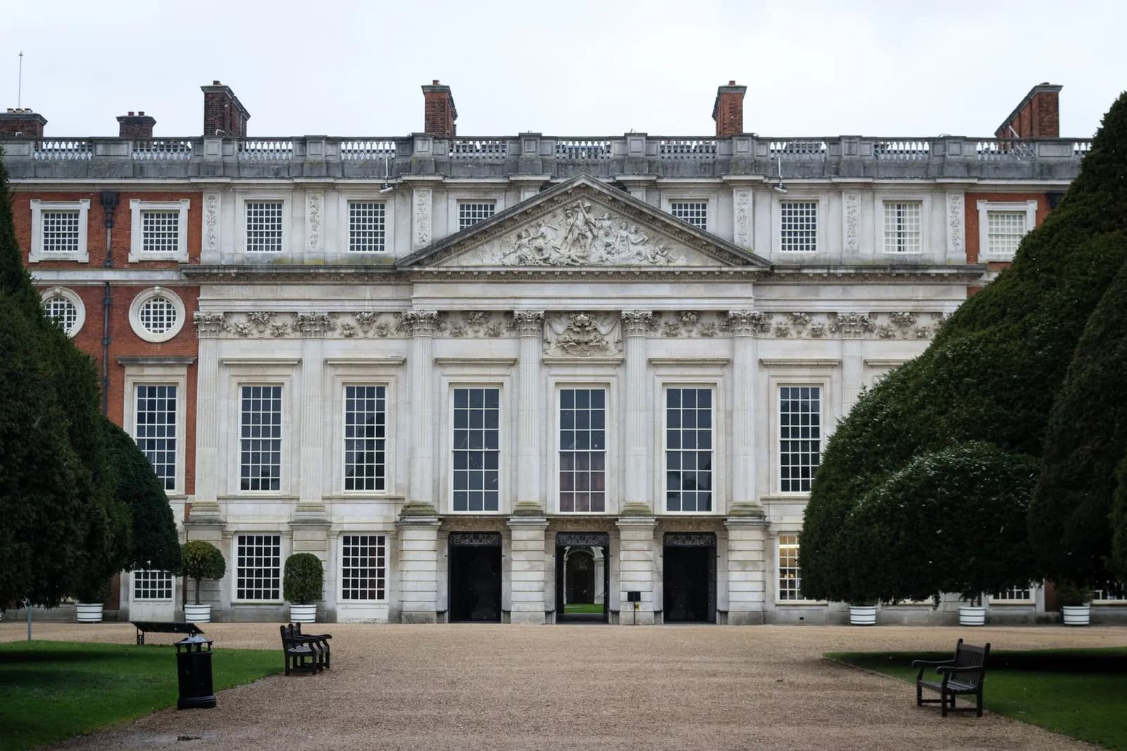 Façade baroque en pierre claire et brique rouge de Hampton Court Palace, entre des ifs taillés