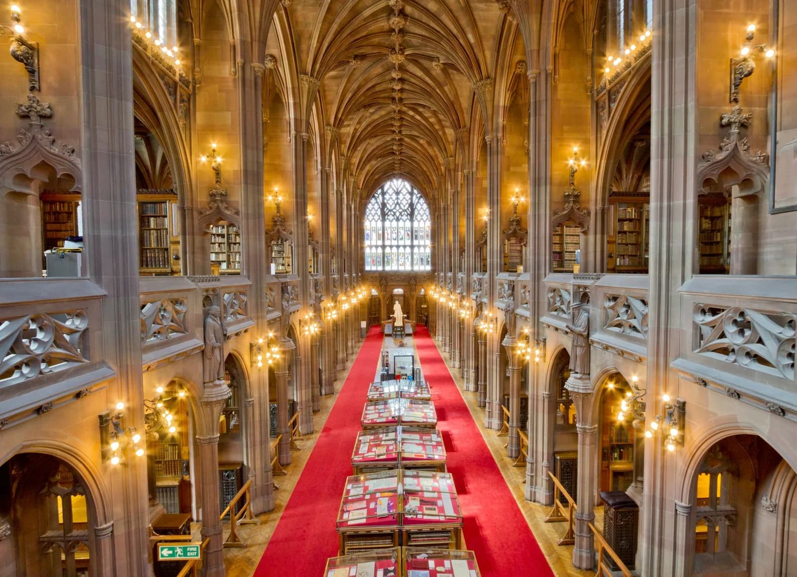 Salle de lecture néogothique de la John Rylands Library à Manchester, avec ses voûtes, ses lampes et son tapis rouge
