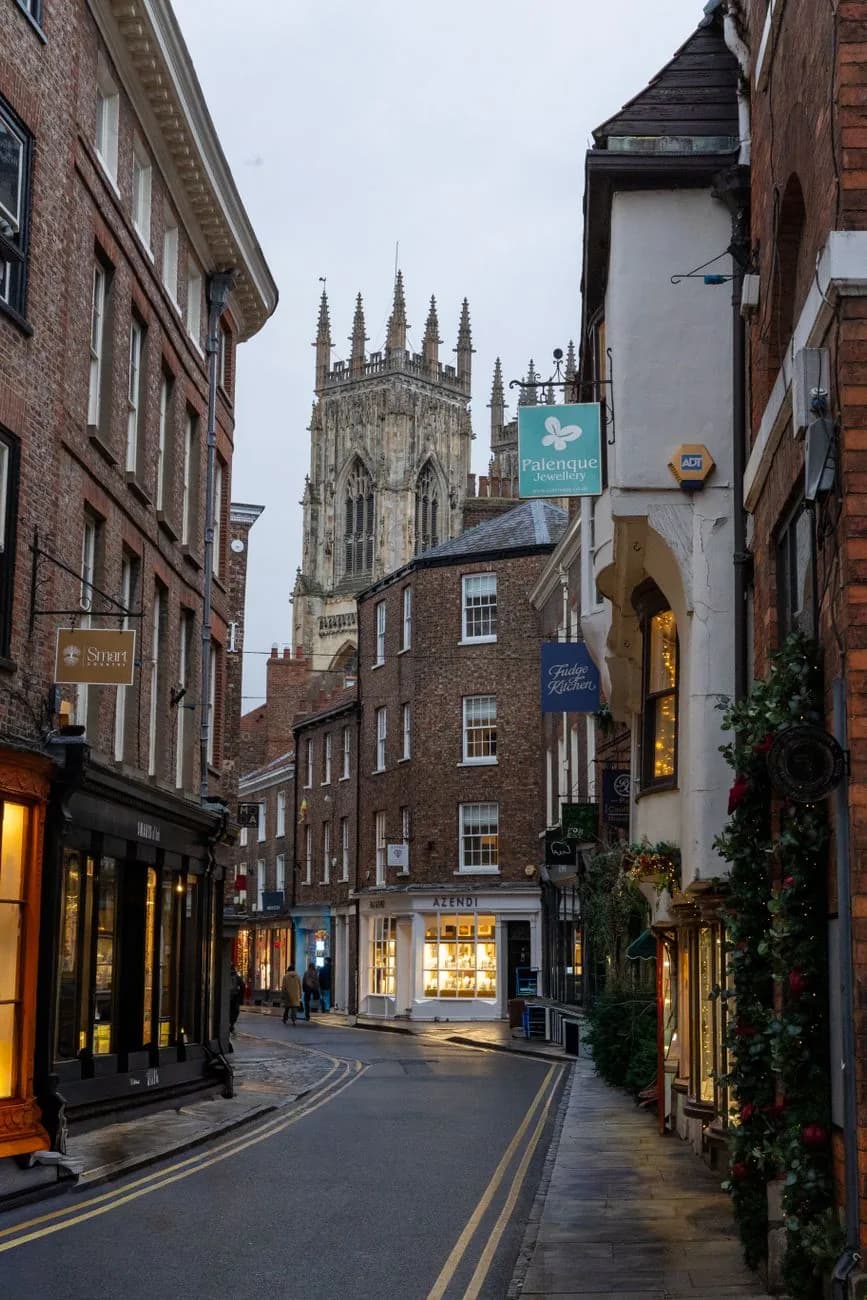 Rue commerçante de York bordée de maisons anciennes, avec la tour du Minster au fond