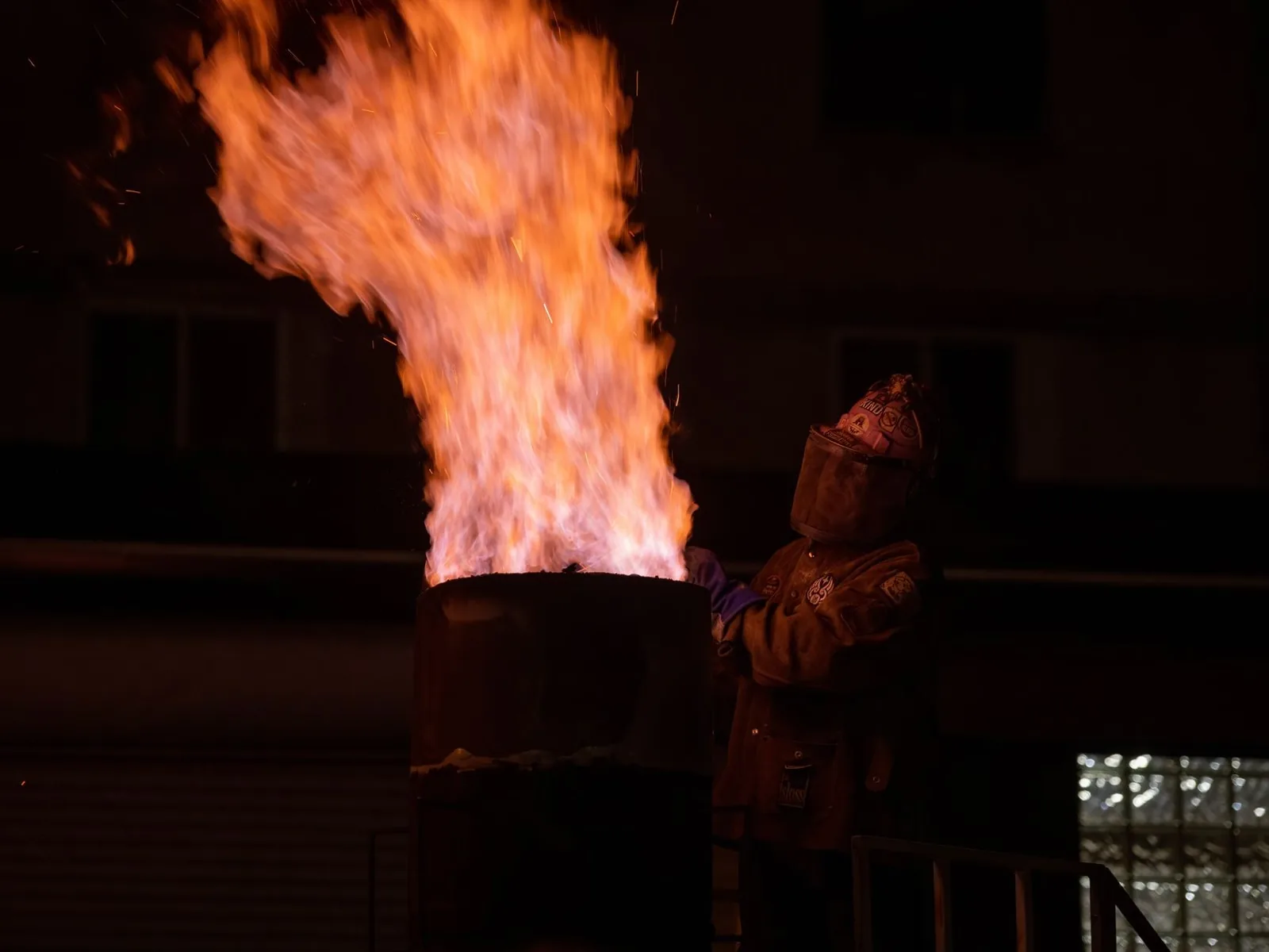 Baril d'où jaillit une haute flamme, dans une rue de nuit