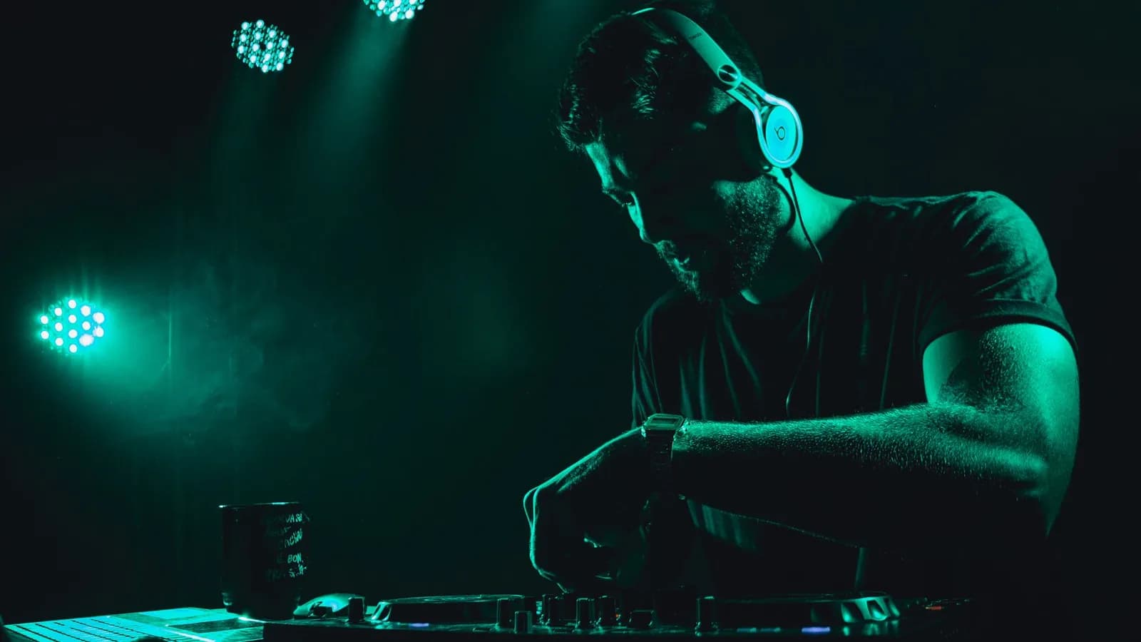 Un DJ au casque derrière sa table de mixage, dans un club sombre