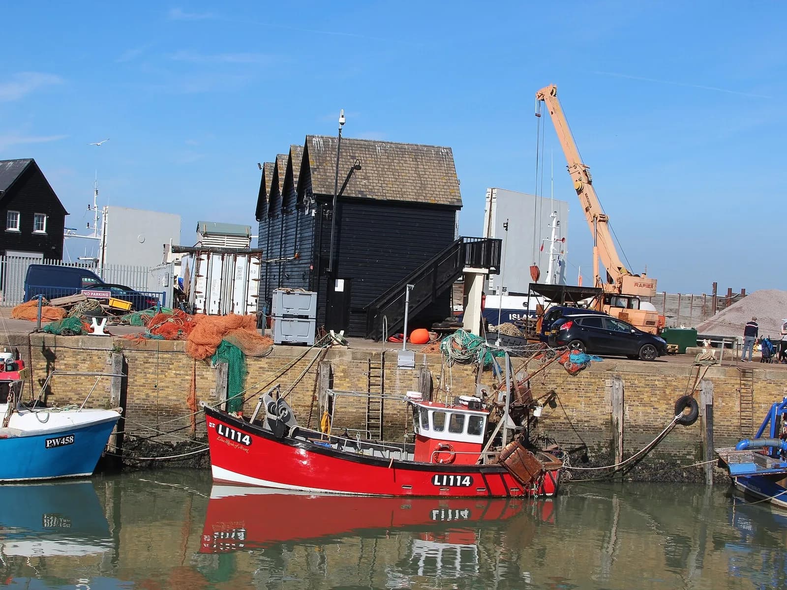 Un chalutier amarré devant les cabanes de pêcheurs en bois noir du port de Whitstable
