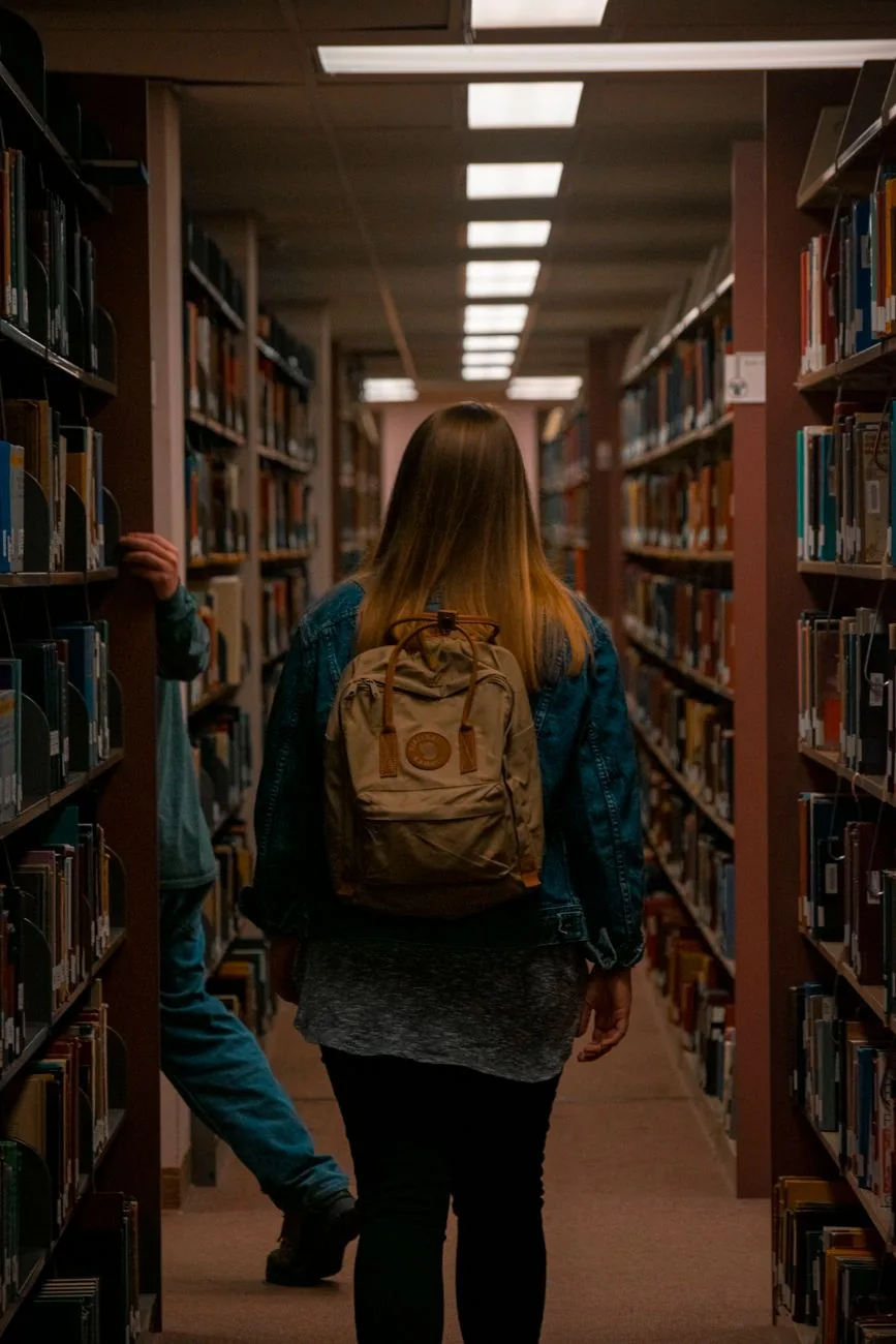 Une personne avec un sac à dos parcourt les rayonnages d'une bibliothèque universitaire