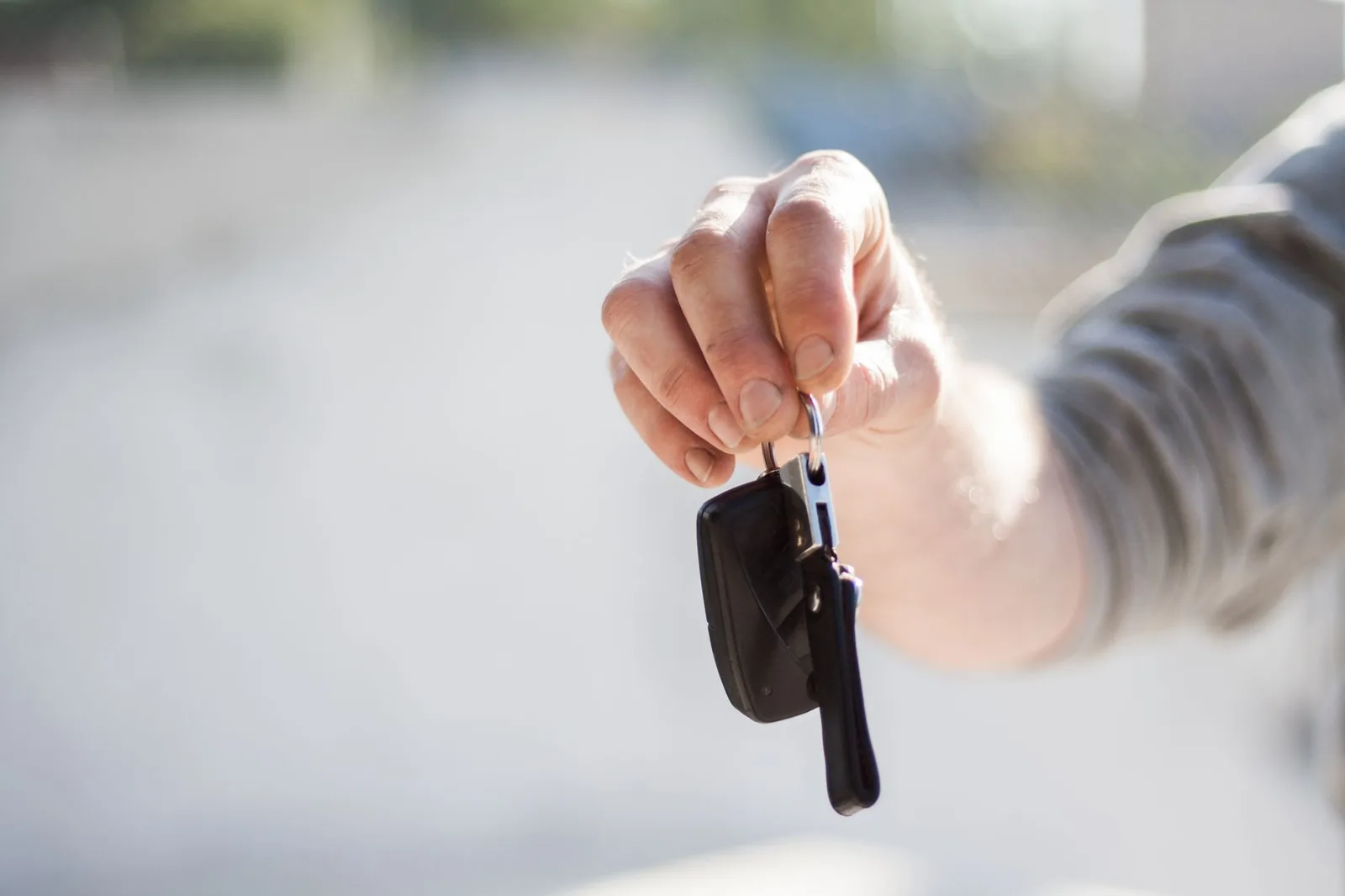 Main tendant une clé de voiture à télécommande, fond clair flou
