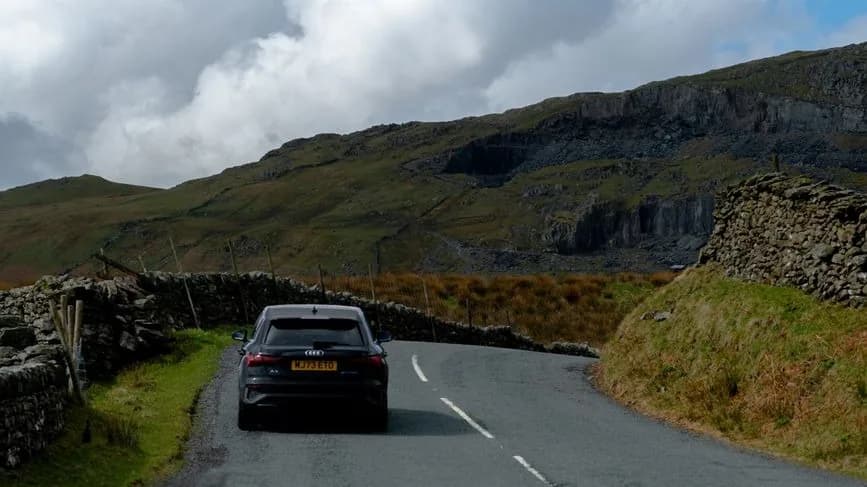 Voiture noire dans un virage d'une route de montagne bordée de murets en pierre sèche, dans le nord de l'Angleterre