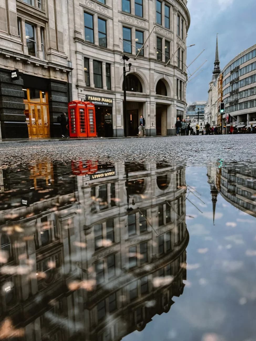 Rue de Londres après une averse, bâtiments reflétés dans une flaque, cabines téléphoniques rouges