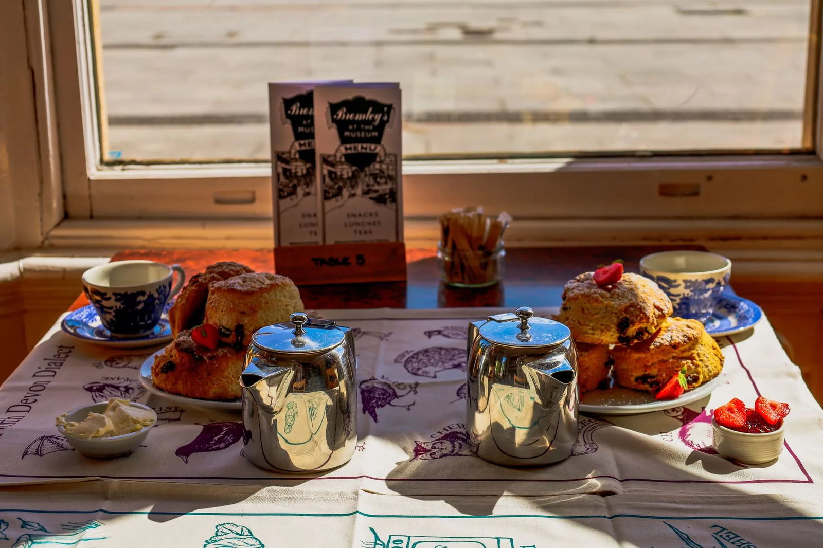 Scones servis avec de la crème épaisse, de la confiture de fraises et des tasses de thé en porcelaine