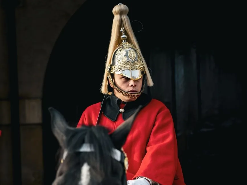 Sentinelle montée de la Household Cavalry en tunique rouge, casque à crinière blanche et cuirasse, devant une porte voûtée sombre