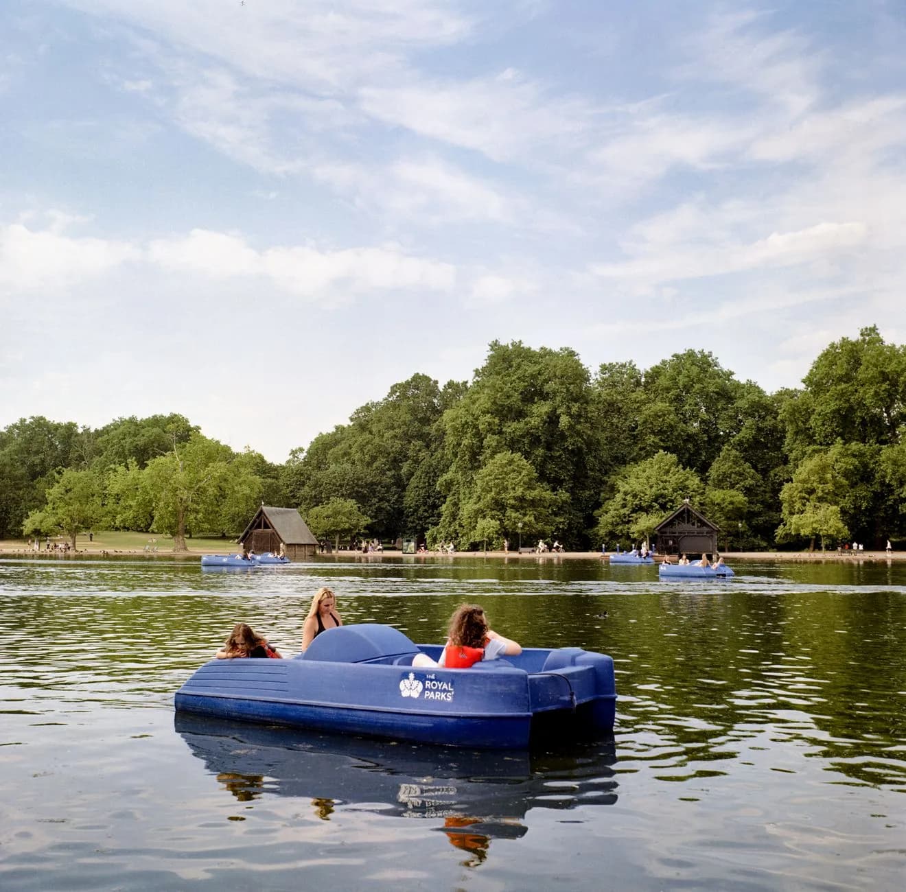 Deux personnes sur un pédalo bleu sur le lac du Serpentine, à Hyde Park, devant les arbres de la rive
