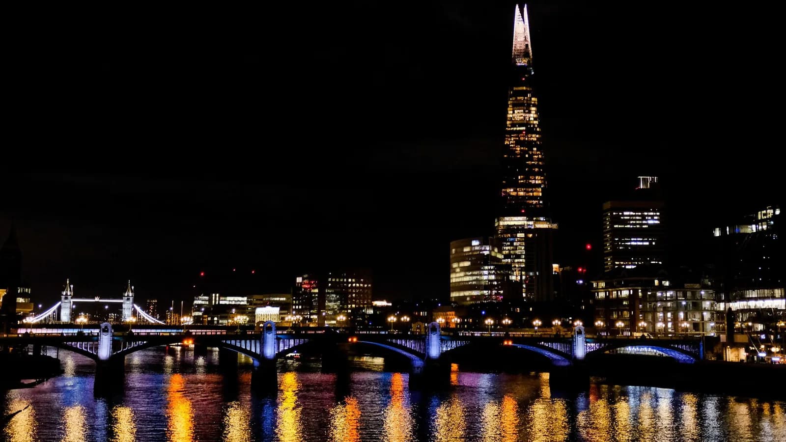 The Shard illuminé de nuit au-dessus de la Tamise, avec Southwark Bridge et Tower Bridge éclairés et leurs reflets sur l'eau