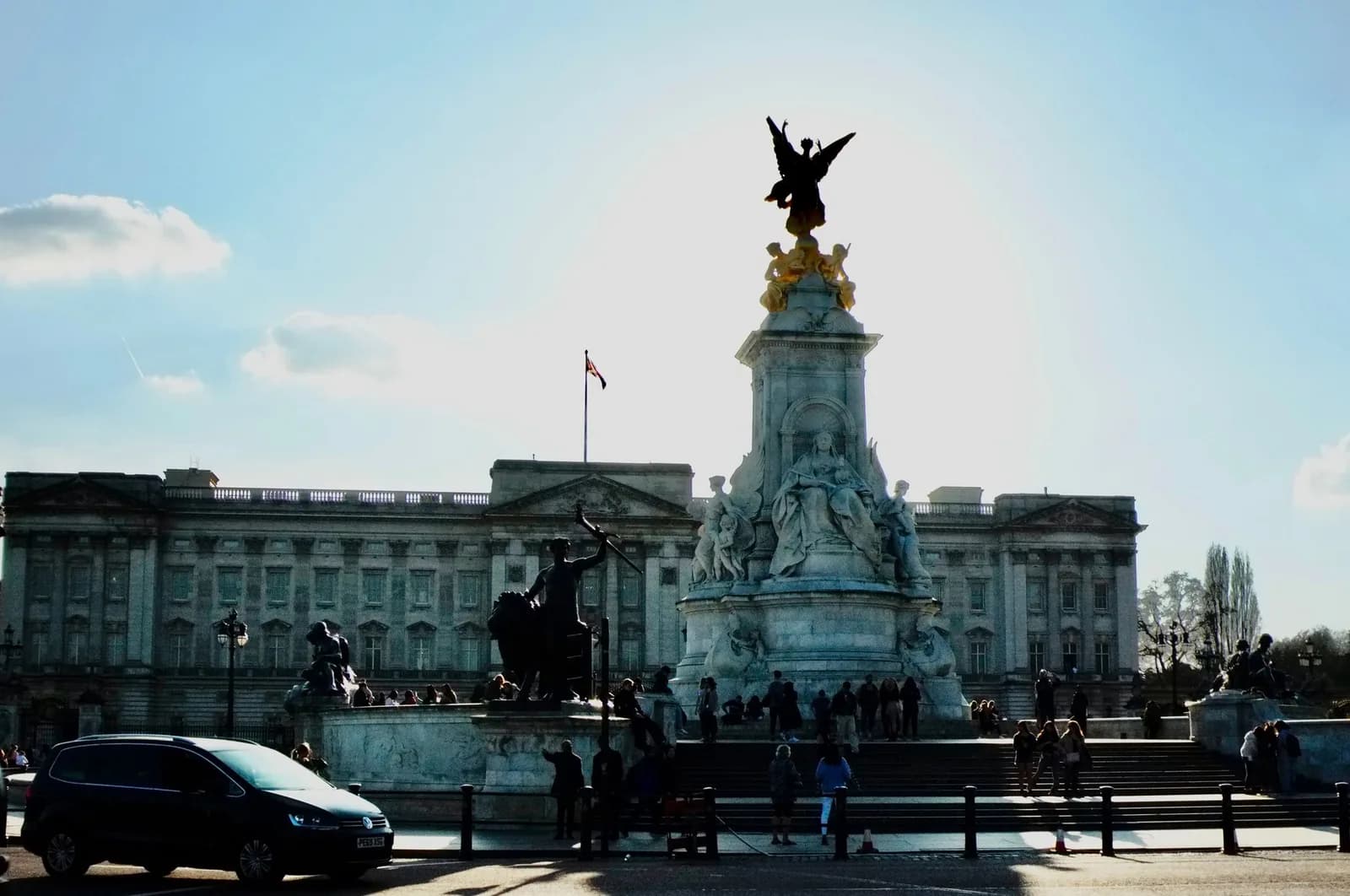 Le Victoria Memorial devant la façade de Buckingham Palace, à contre-jour, avec des visiteurs au pied du monument