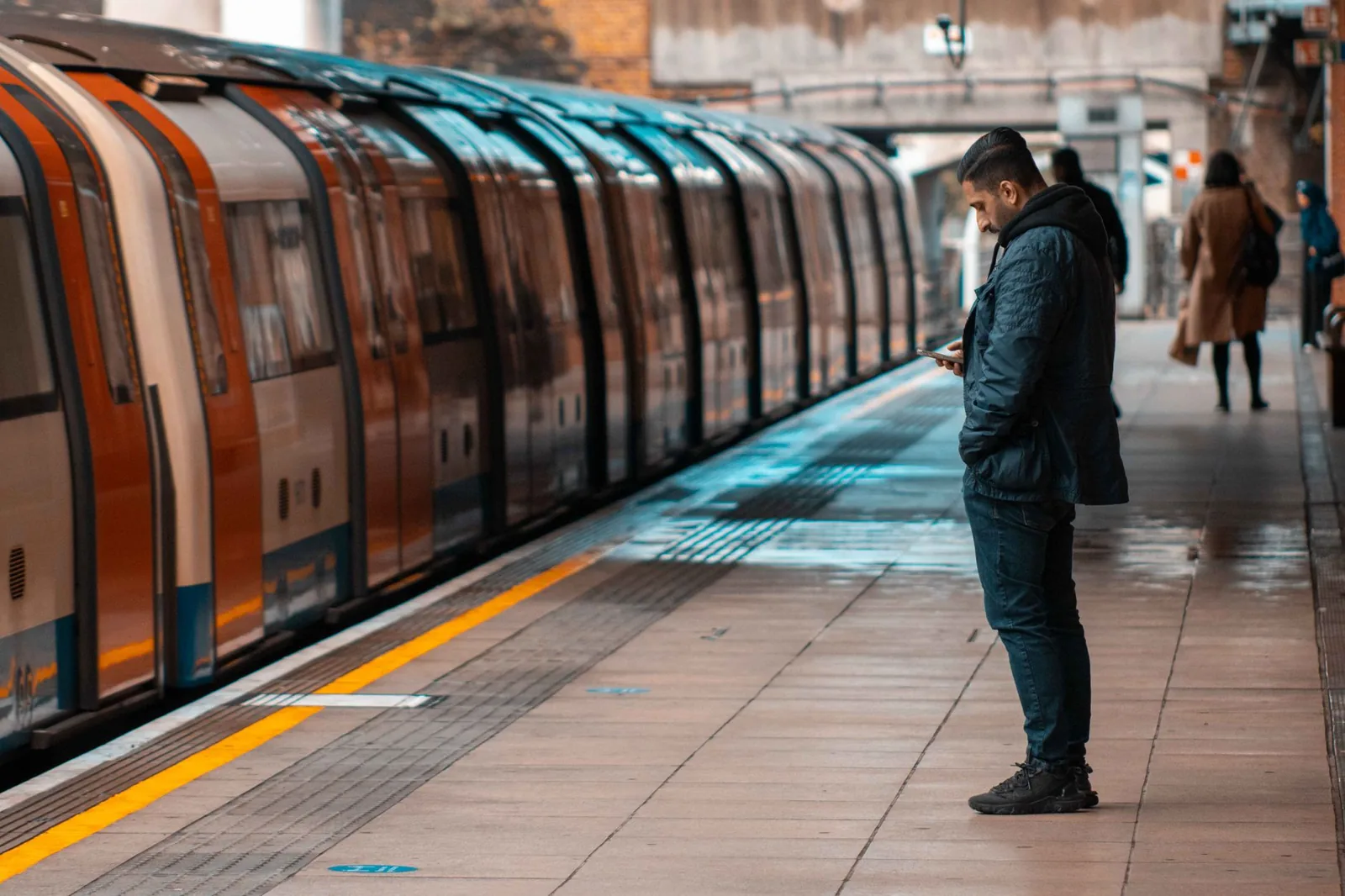 Voyageur regardant son smartphone sur un quai du métro de Londres devant une rame de l'Underground
